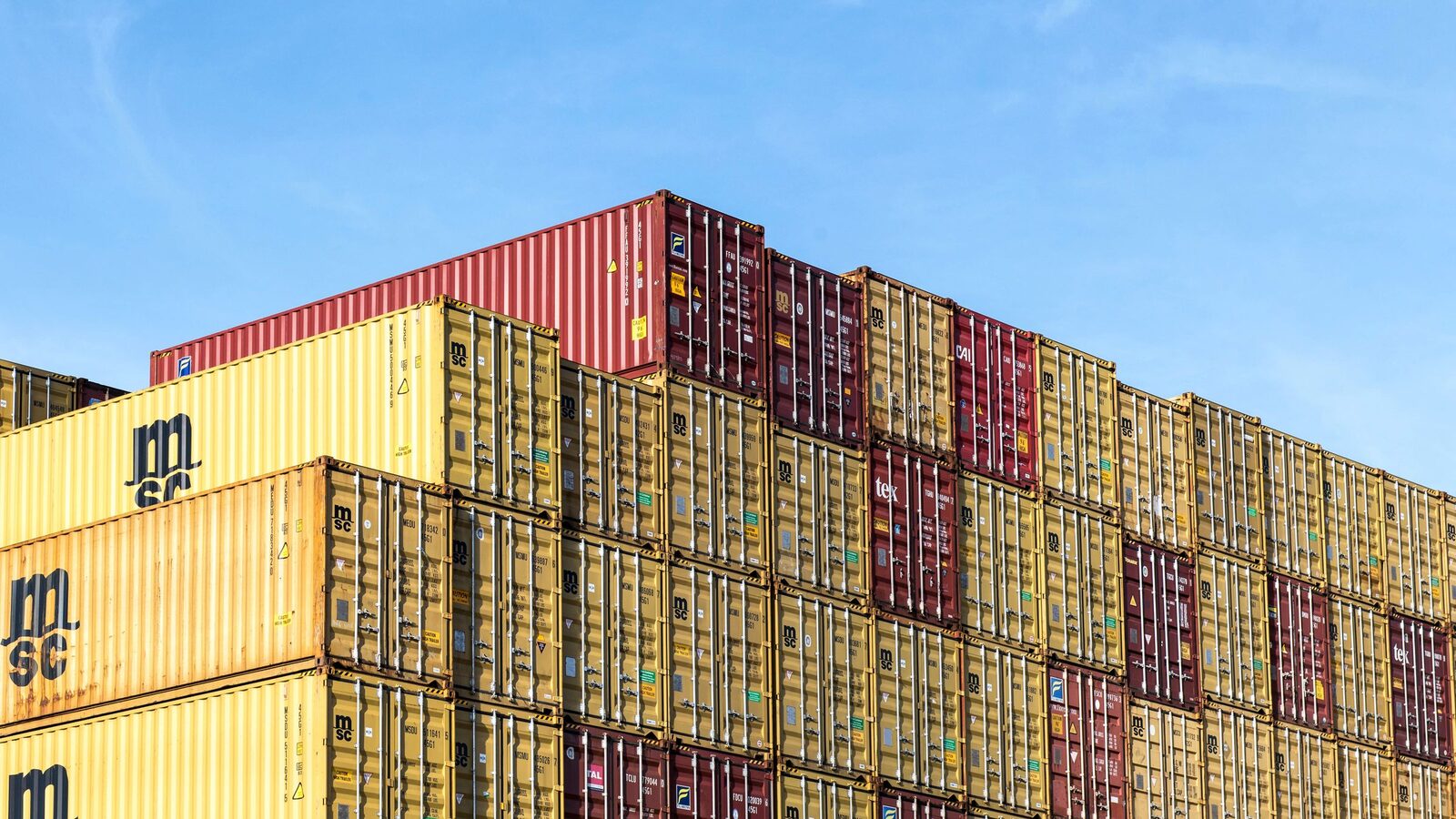 Stacked shipping containers at a port under a clear sky