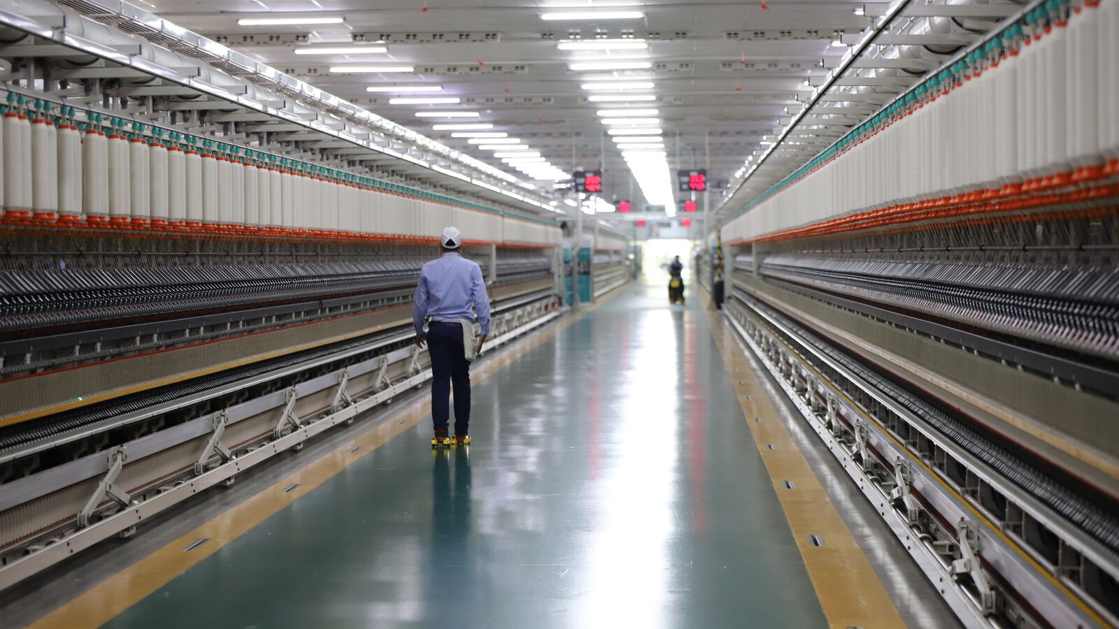 Worker walking the aisle of an industrial textile plant between rows of machines